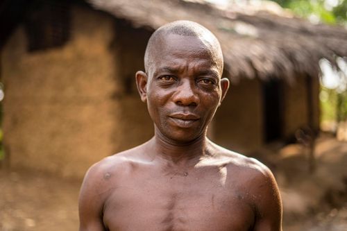 Free Close-up portrait of an African man standing outdoors in a village setting. Stock Photo