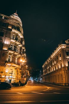 A quiet city street at night featuring grand architectural buildings illuminated with lights.