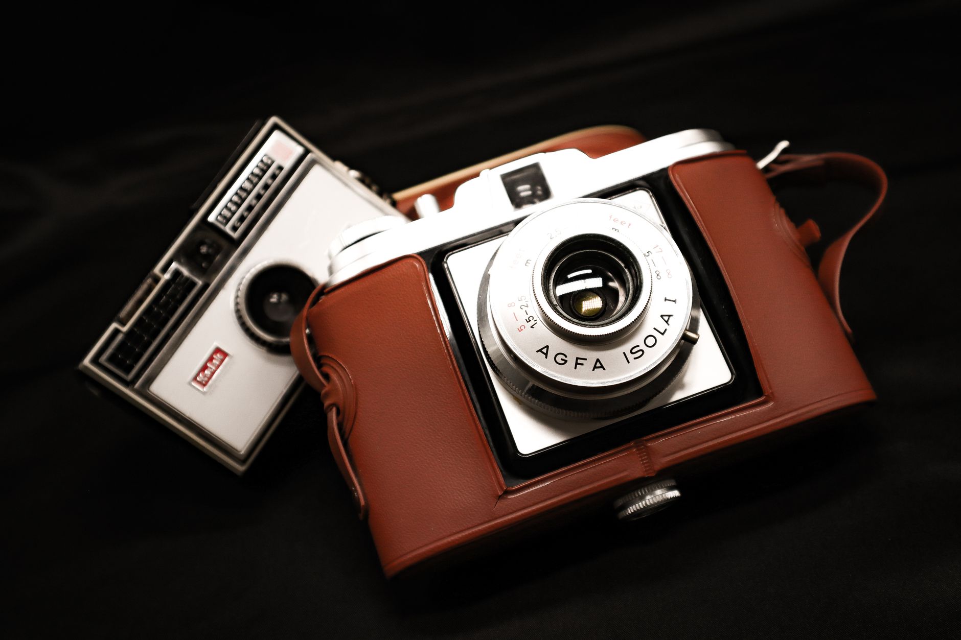 Close-up of vintage AGFA and other classic cameras with leather cases on a dark background.