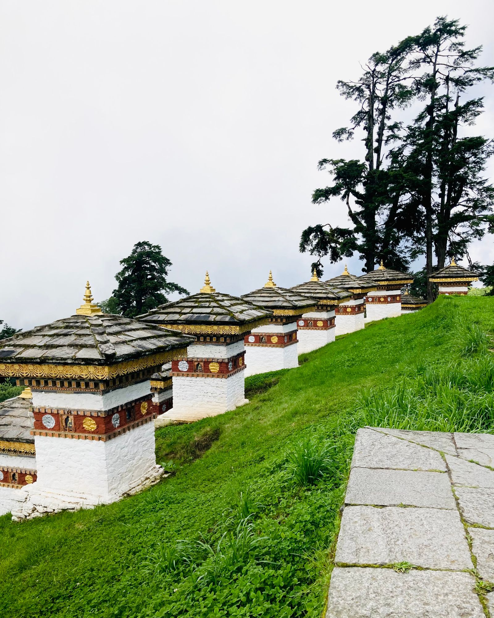 Druk Wangyal chortens at Dochu La climbing a green slope in tiers, the pass wrapped in white cloud