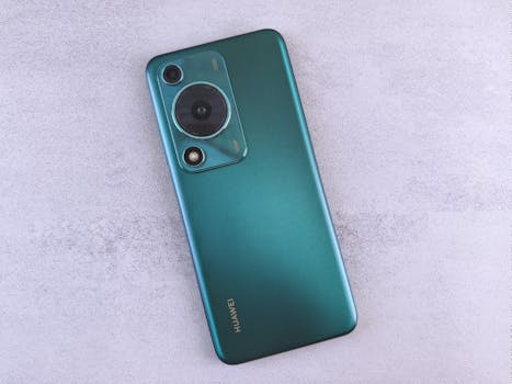 Close-up of a sleek green smartphone with dual camera on a textured light surface.