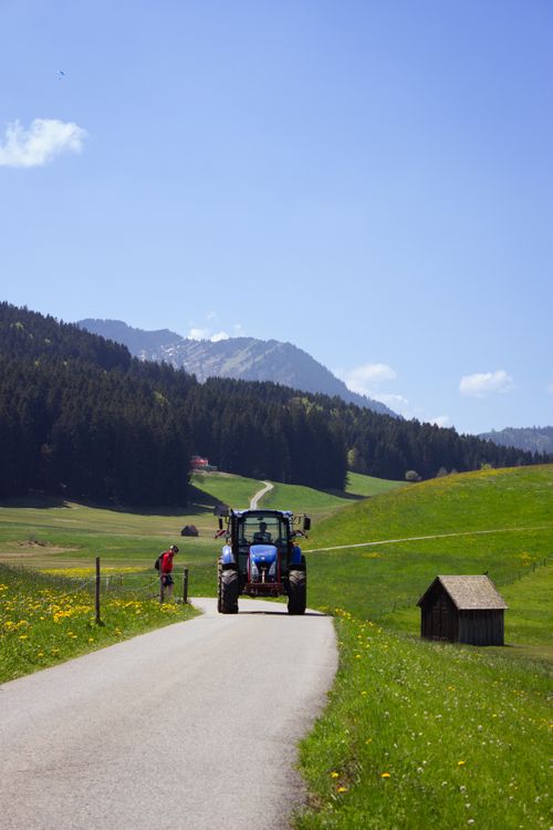 Free Tractor travels along a picturesque mountain road in Switzerland's lush countryside under a bright sky. Stock Photo