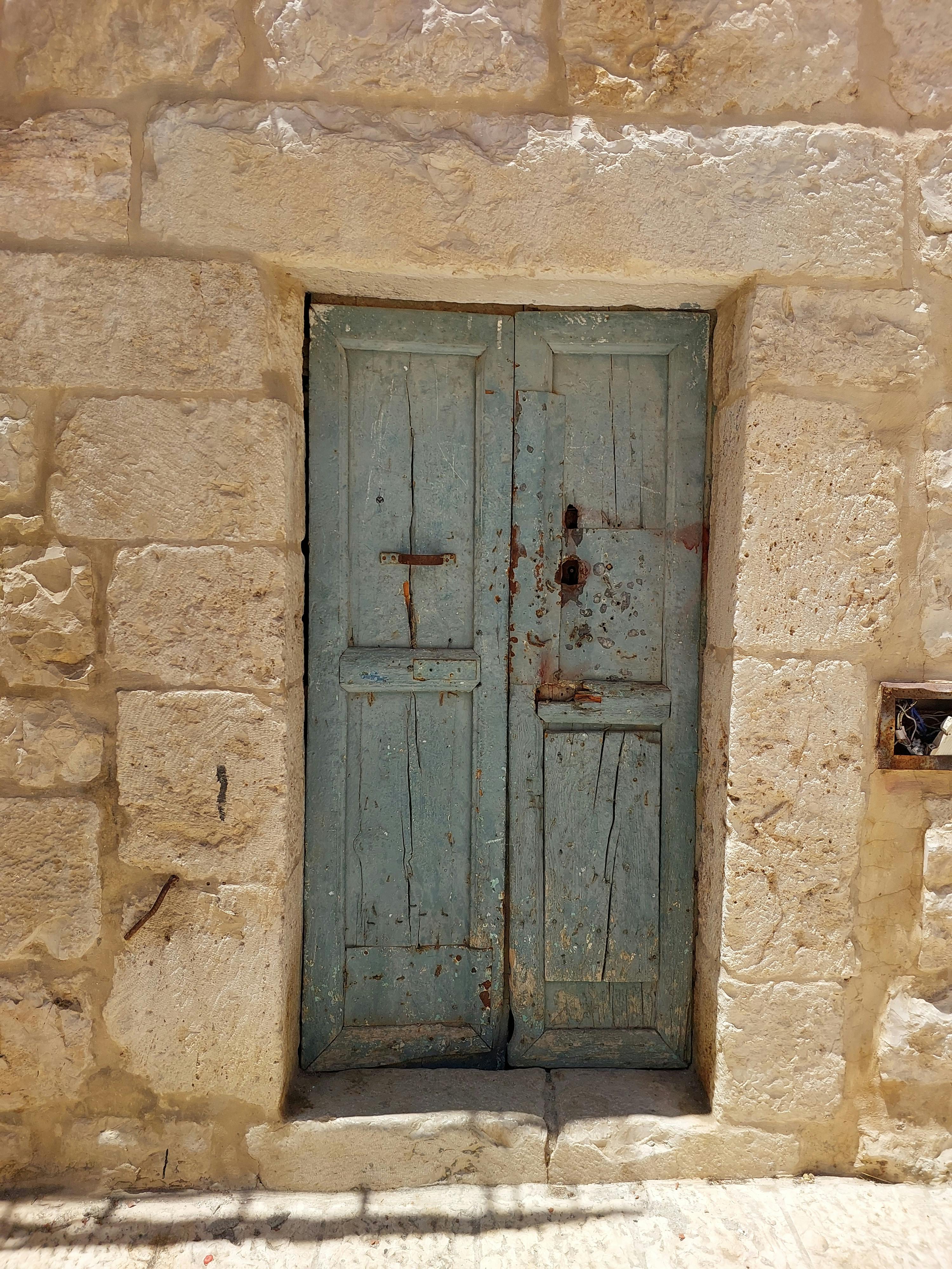 Explore the textured charm of an old blue door set in Bethlehem's historic stone walls.