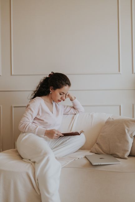 A young woman enjoys reading a book on a comfortable couch indoors, with natural lighting creating a warm ambiance.