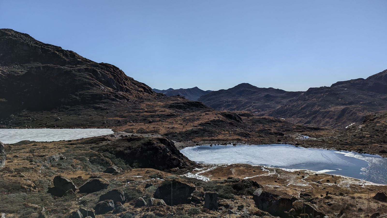Frozen high altitude tarns among dark rocky knolls and brown winter grass at Kupup in East Sikkim, close under the old Jelep La