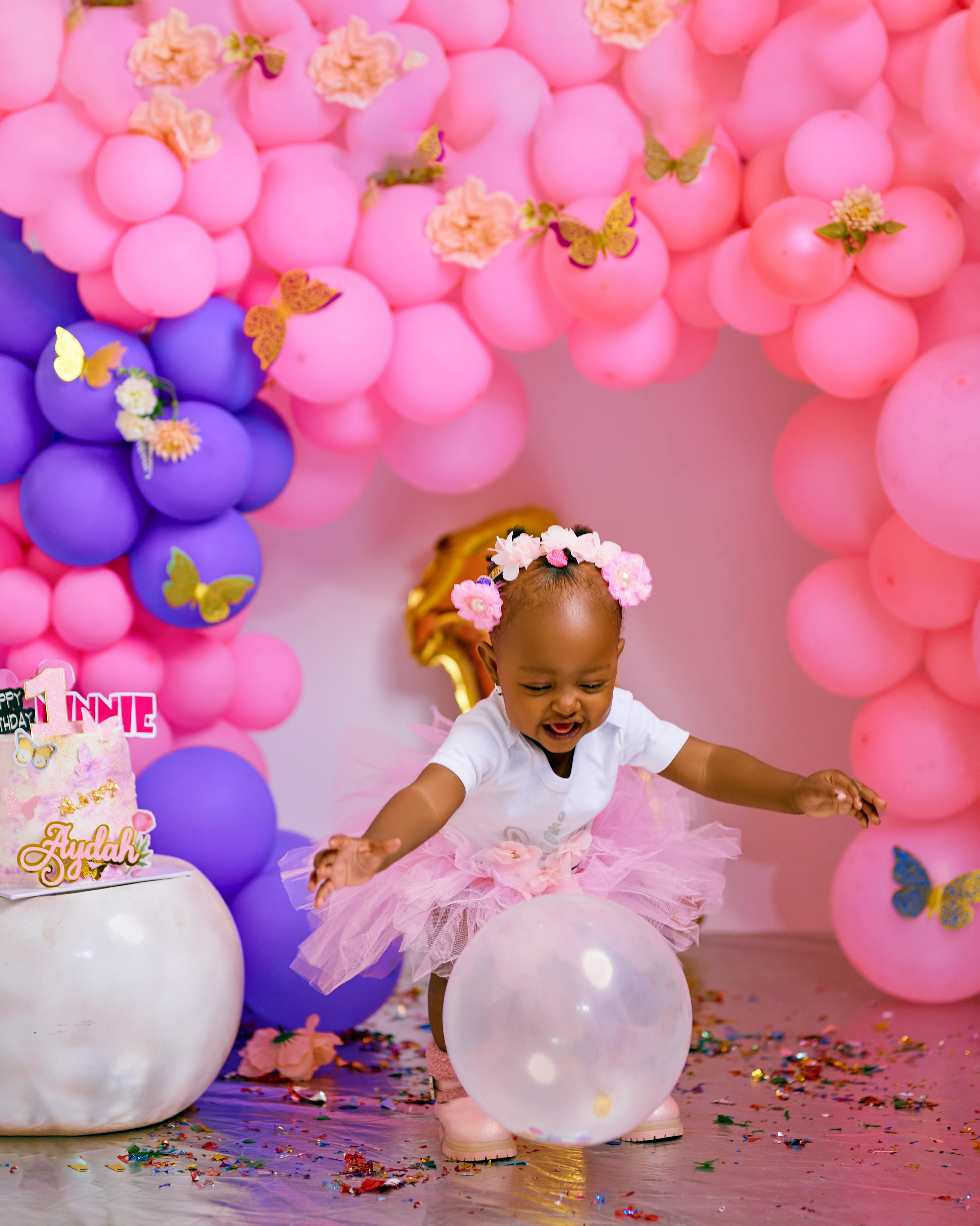 Adorable baby in pink tutu celebrates her birthday with colorful balloons and confetti.