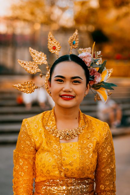 Portrait of a smiling woman in traditional Thai attire with a gold headdress, outdoors in Phuket.