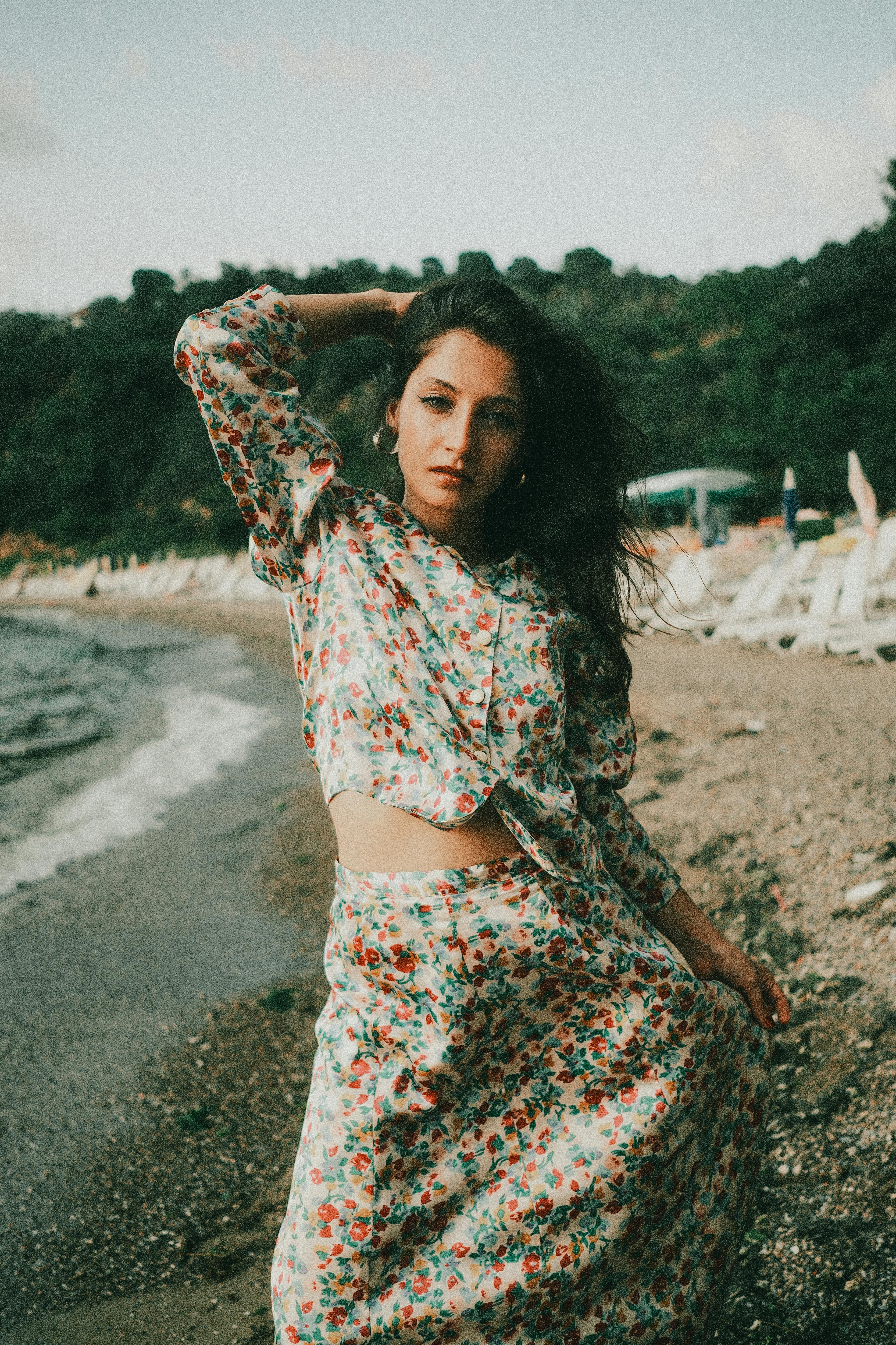 日落时分，一位身着花卉服装的优雅女子在风景如画的海滩上摆姿势，体现夏日气息