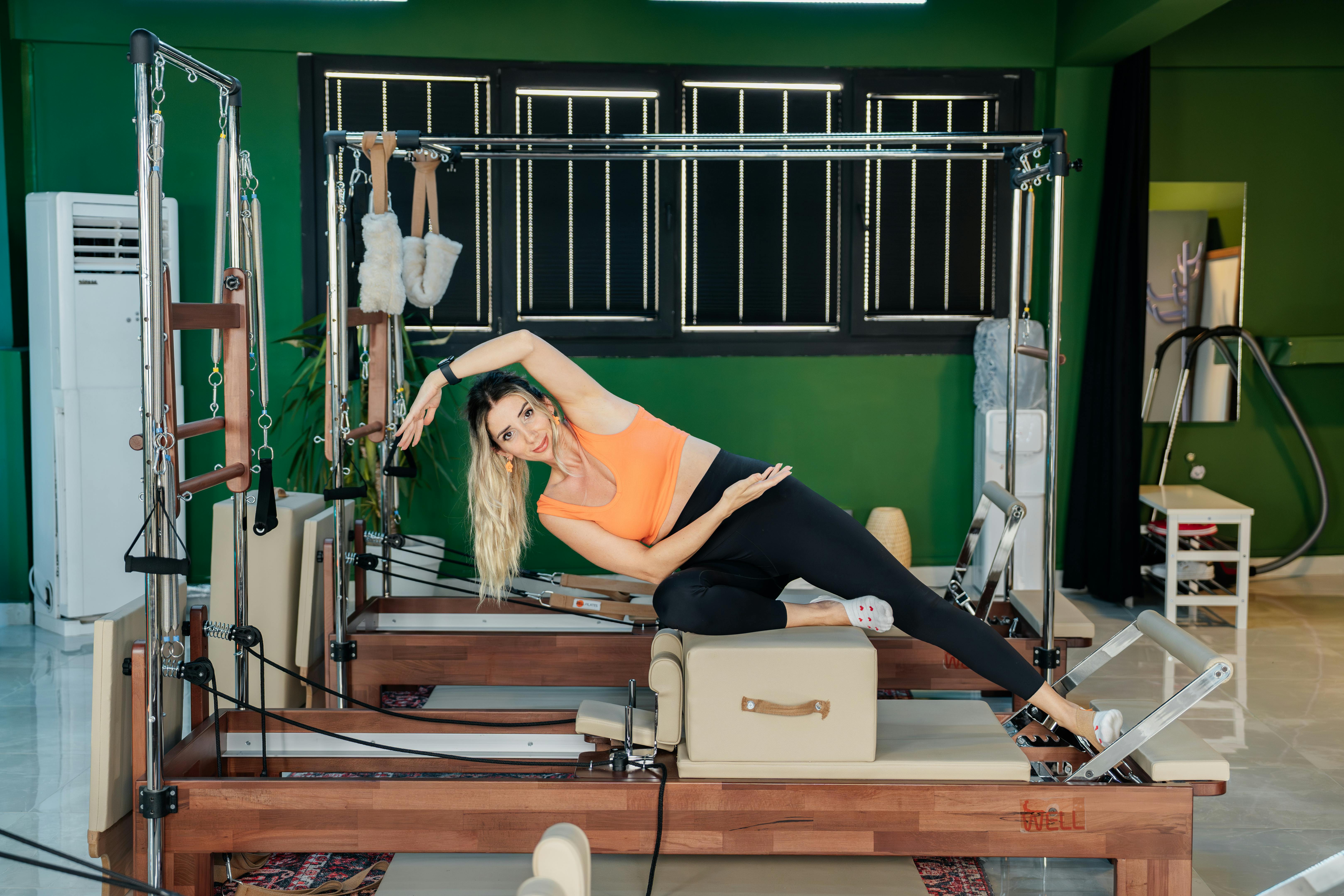 Woman performing side stretch exercise on Pilates reformer machine indoors.