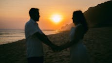 在充满活力的日落时分，海滩上一对情侣手牵着手的浪漫剪影