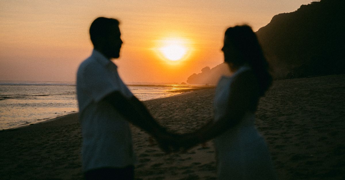 Silhouette of a couple holding hands on a beach at sunset