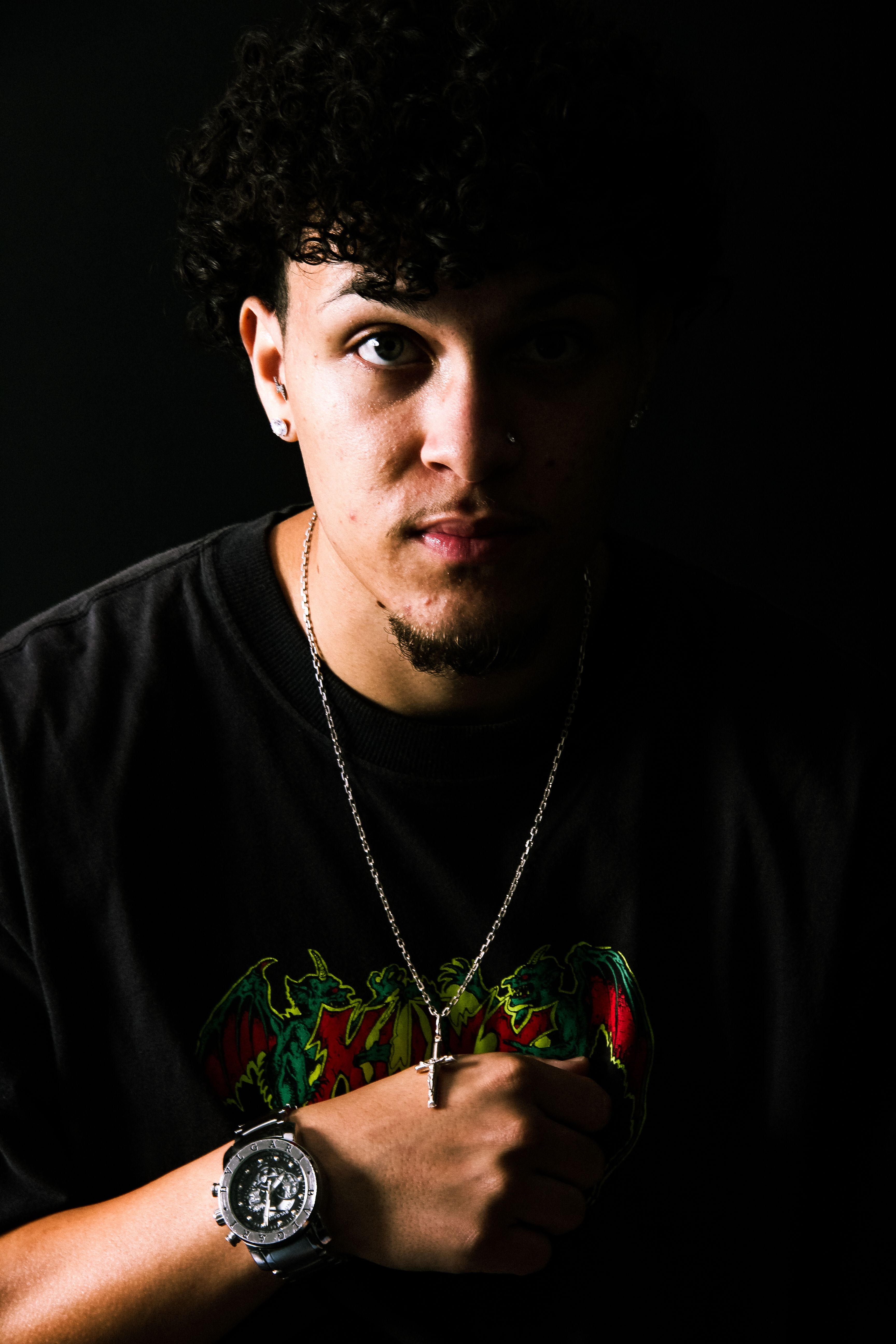 Close-up portrait of a young man with jewelry, striking chiaroscuro lighting.