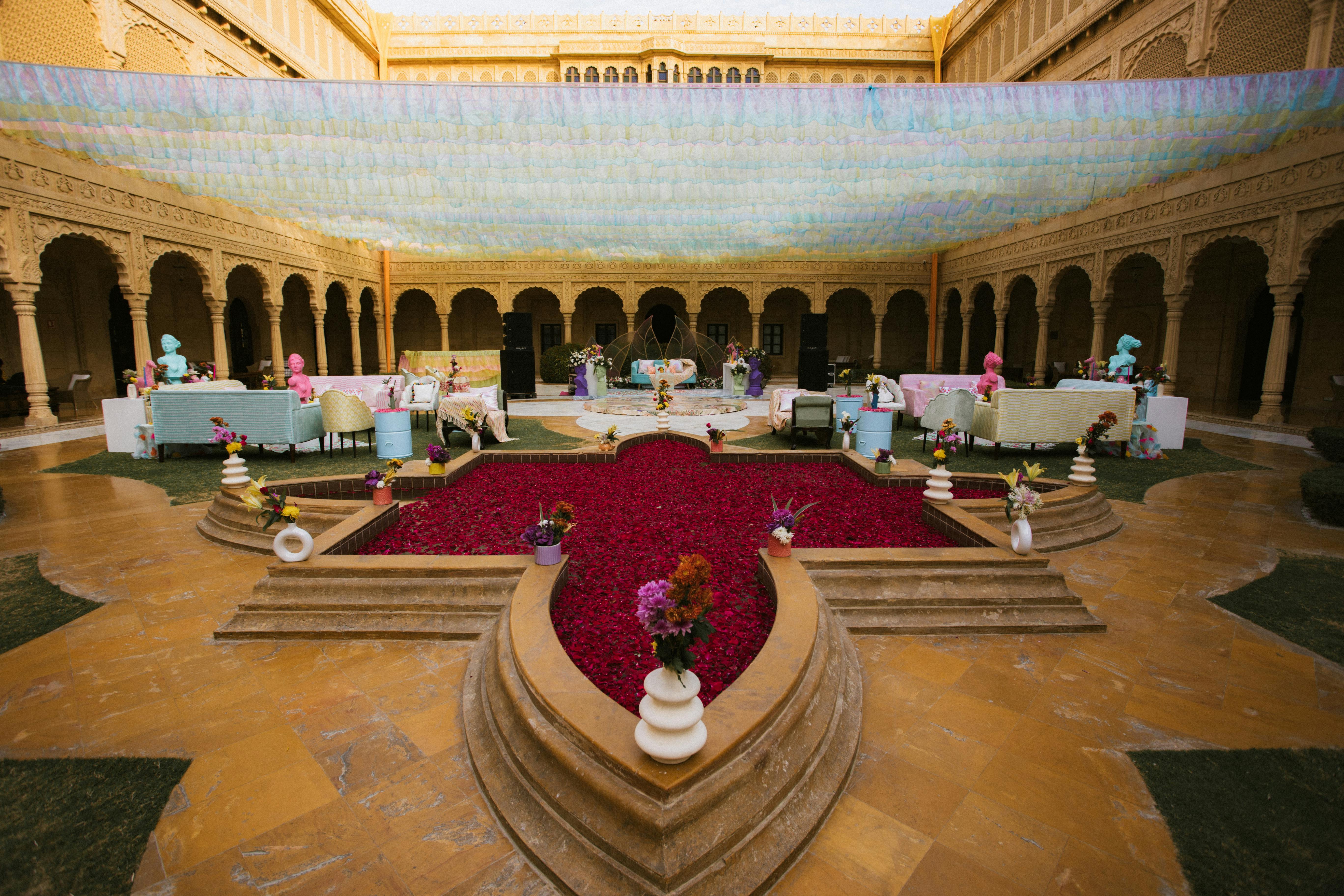 Vibrant courtyard with colorful decor and rose petals, under ornate arches.