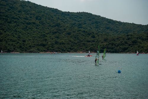 Free Scenic view of windsurfers navigating calm waters with lush green hills in Hong Kong. Stock Photo