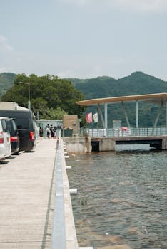 A serene pier in Hong Kong with vehicles parked alongside, overlooking lush green mountains.