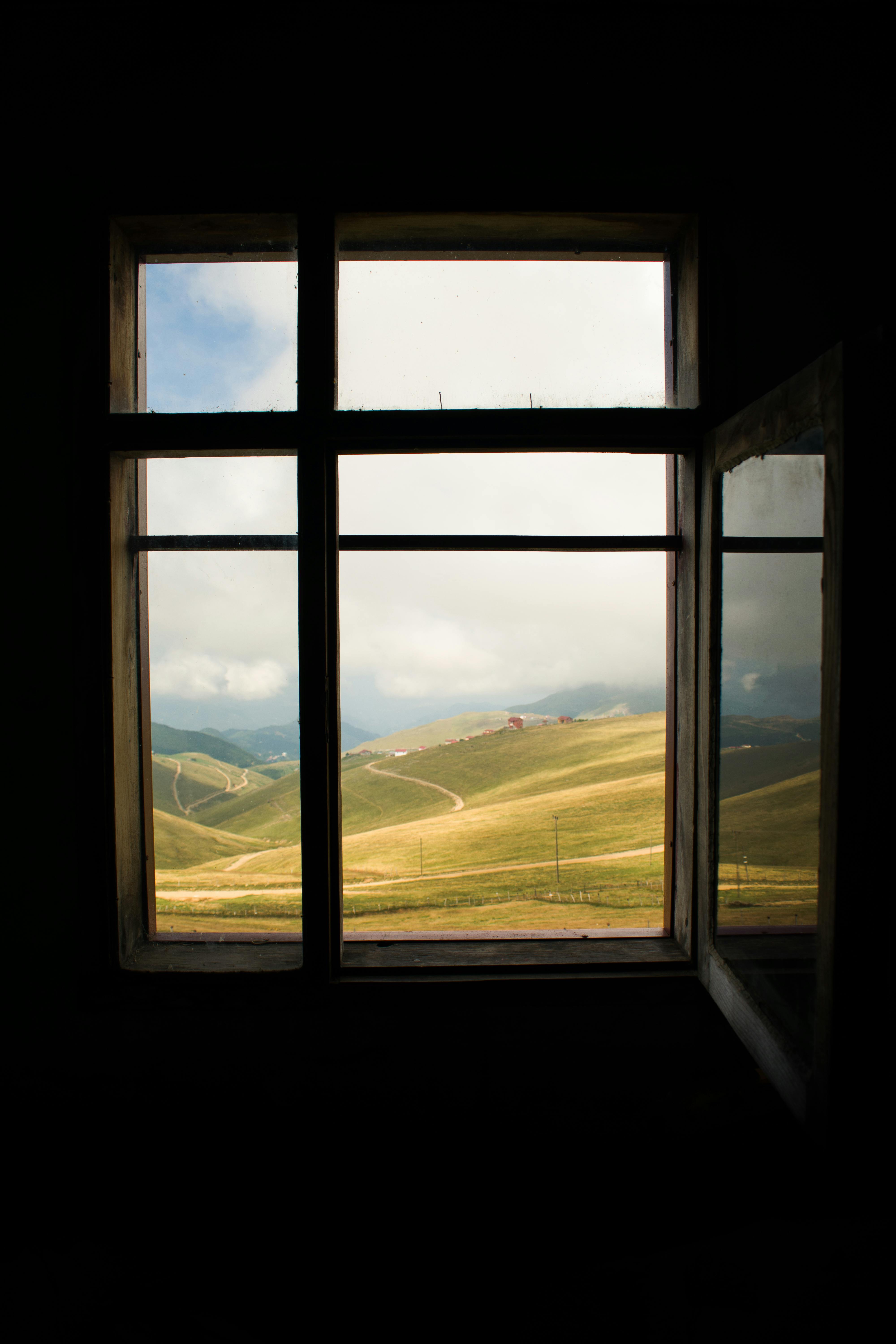 Beautiful mountain landscape seen through an open, rustic window frame, evoking tranquility and appreciation for nature.