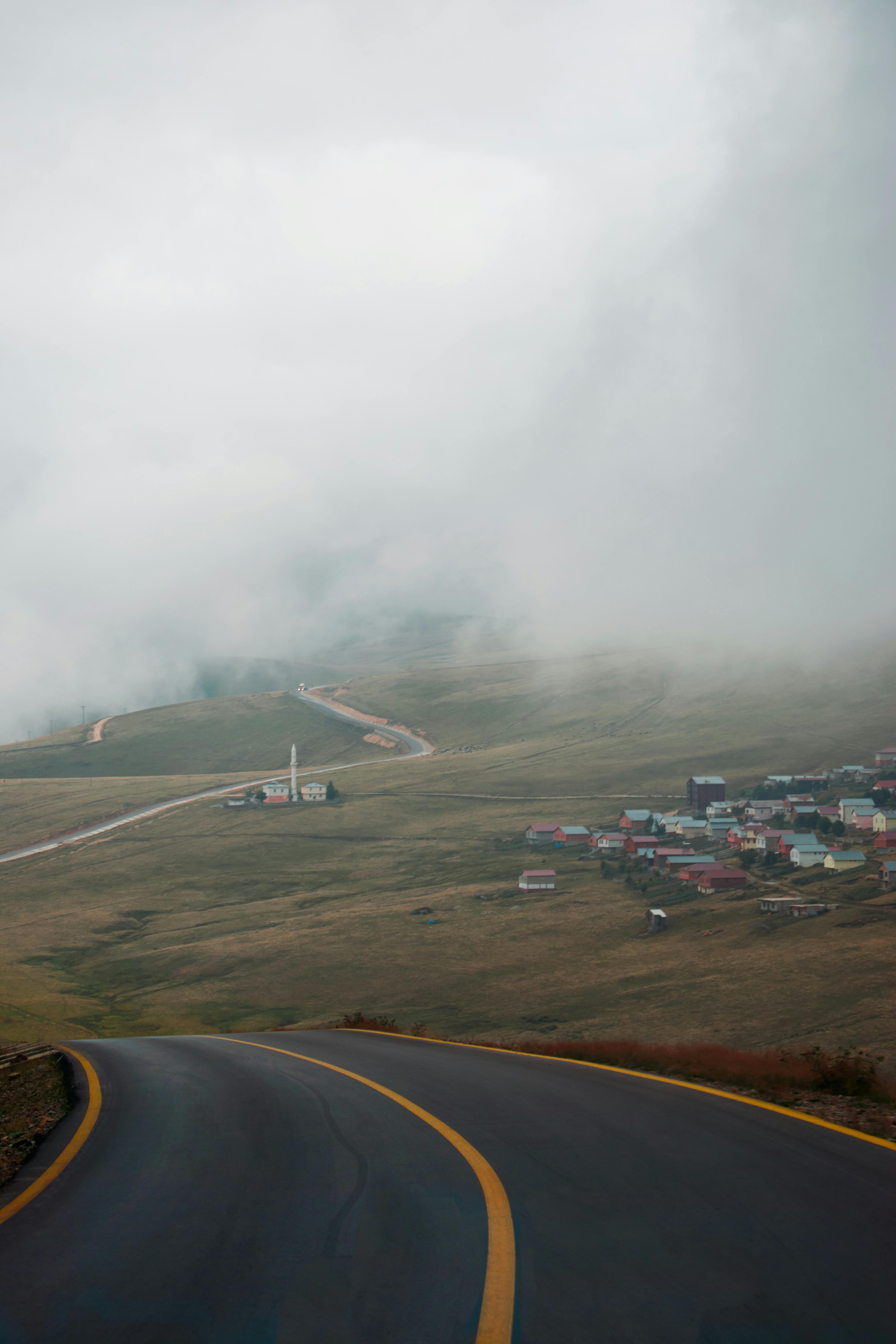 Serene misty landscape featuring a winding road leading to a remote village in an open field.