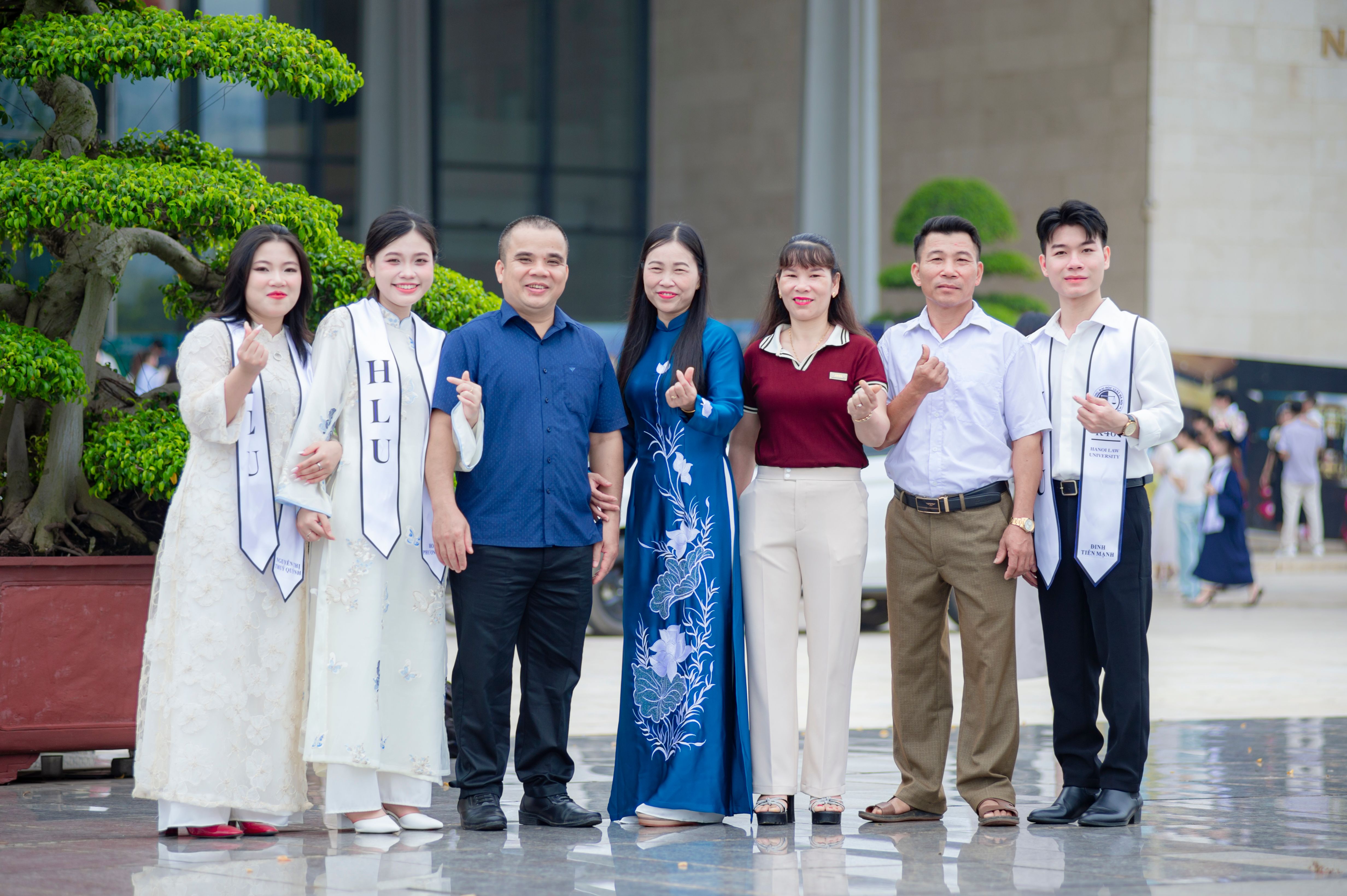 Group of adults in graduation attire posing outside Hanoi Law University, Vietnam.
