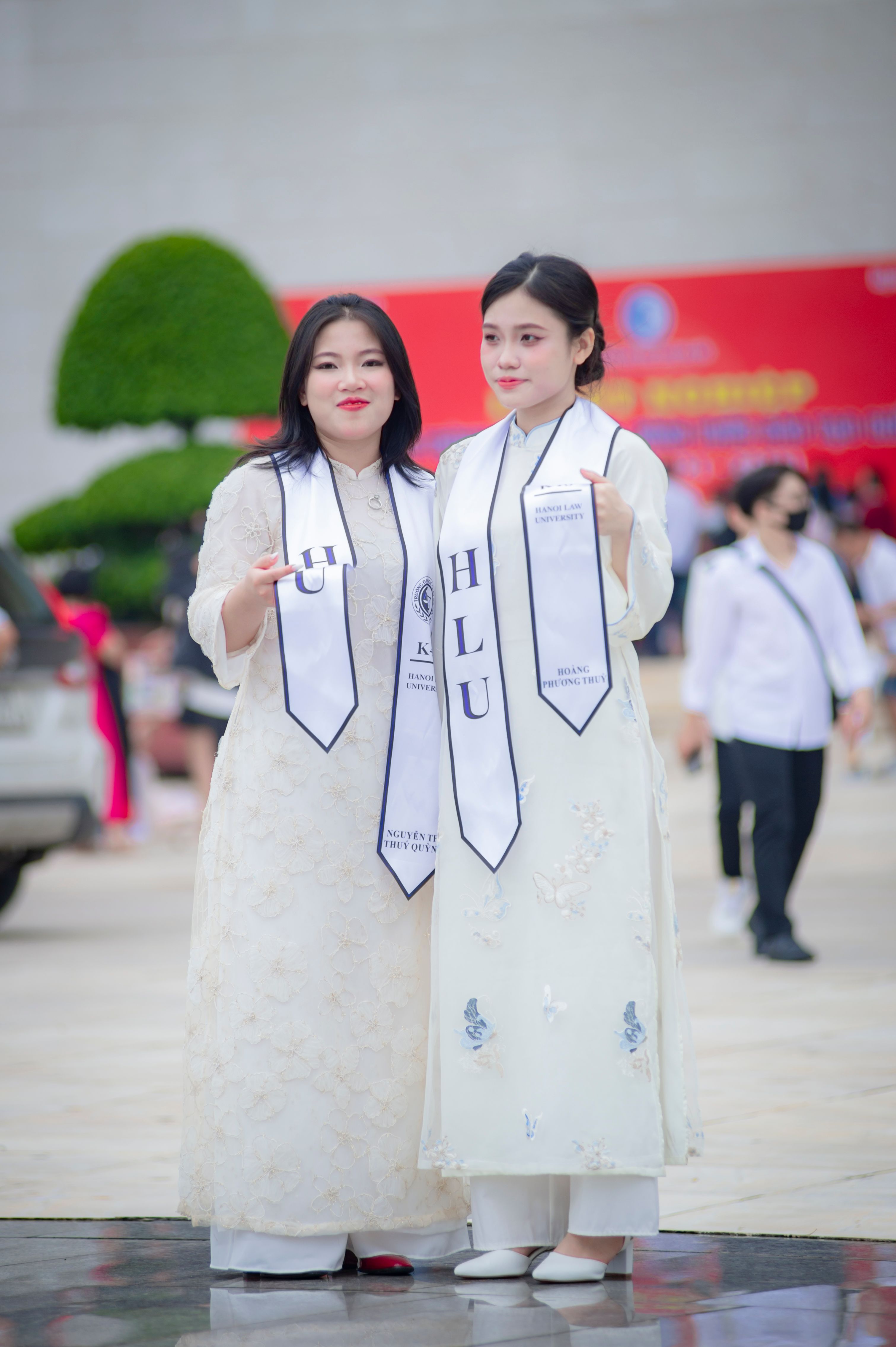 Two women in traditional Vietnamese attire celebrate graduation outdoors in Hanoi, Vietnam.