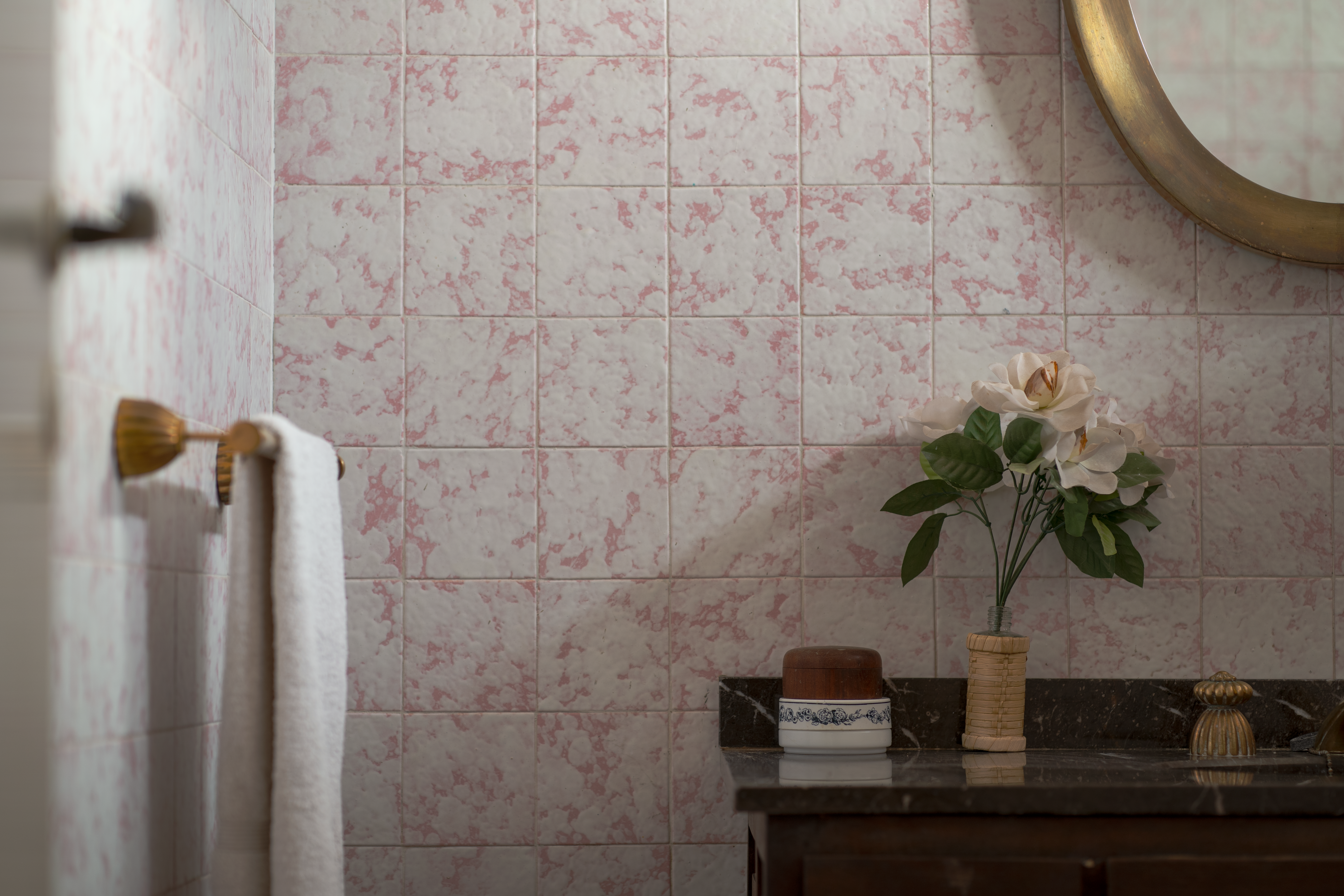 Charming bathroom scene with vintage tiles, a round mirror, and floral decoration.
