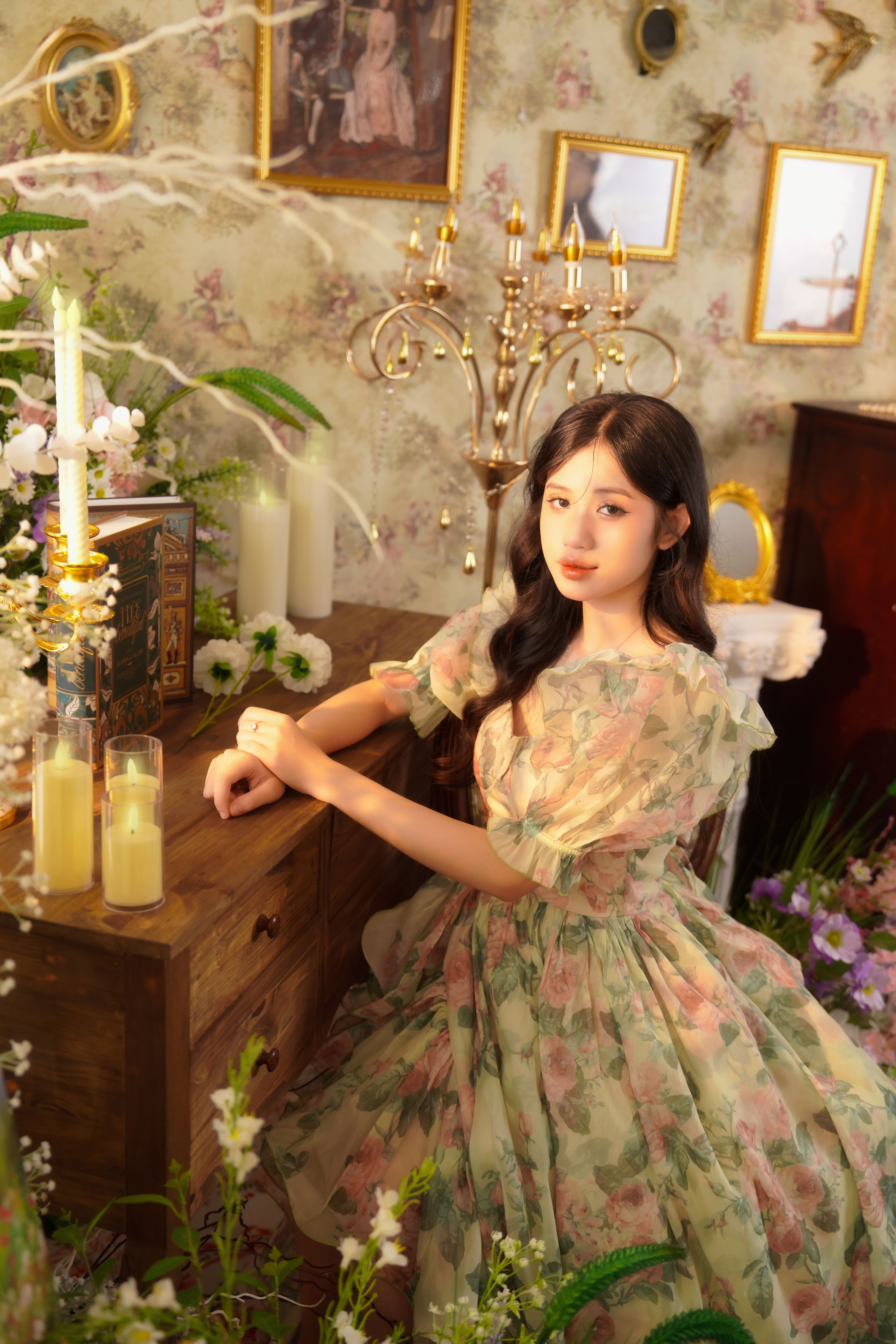 Woman in a floral dress posing in a vintage setting with candles and flowers.