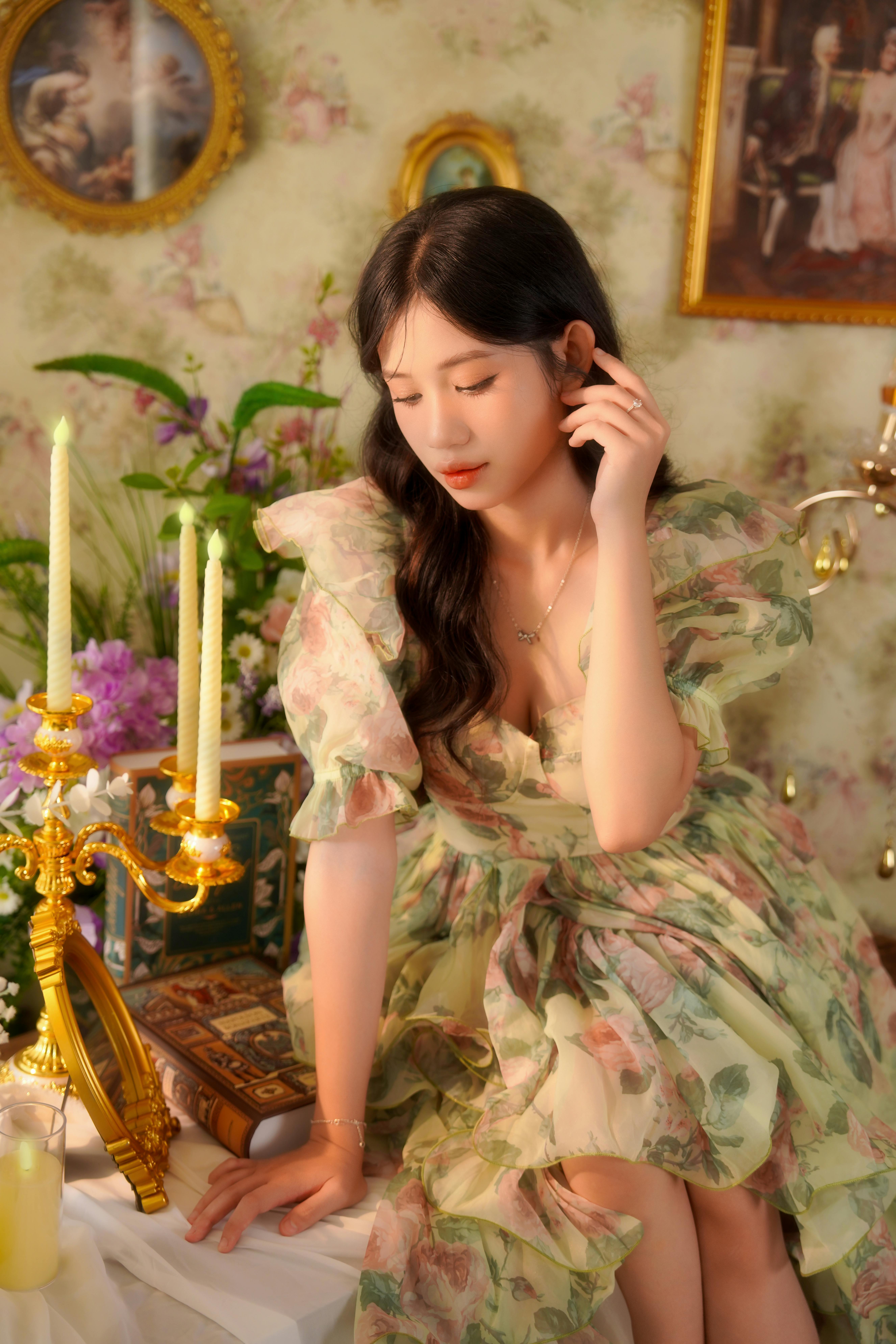 A woman in a vintage floral dress poses elegantly in a decorated room, with warm lighting.