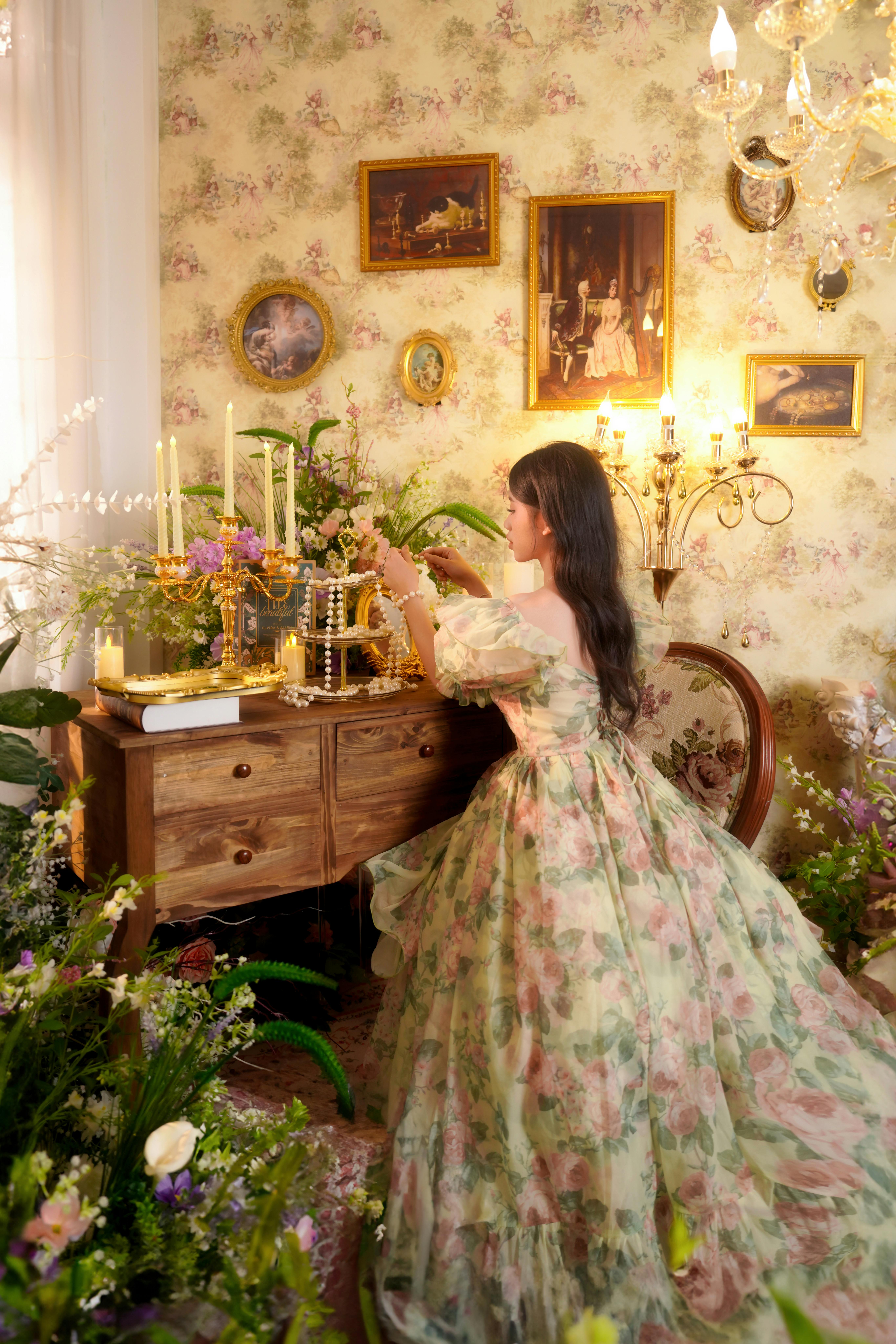 A woman in a floral gown decorates a vintage table surrounded by flowers.