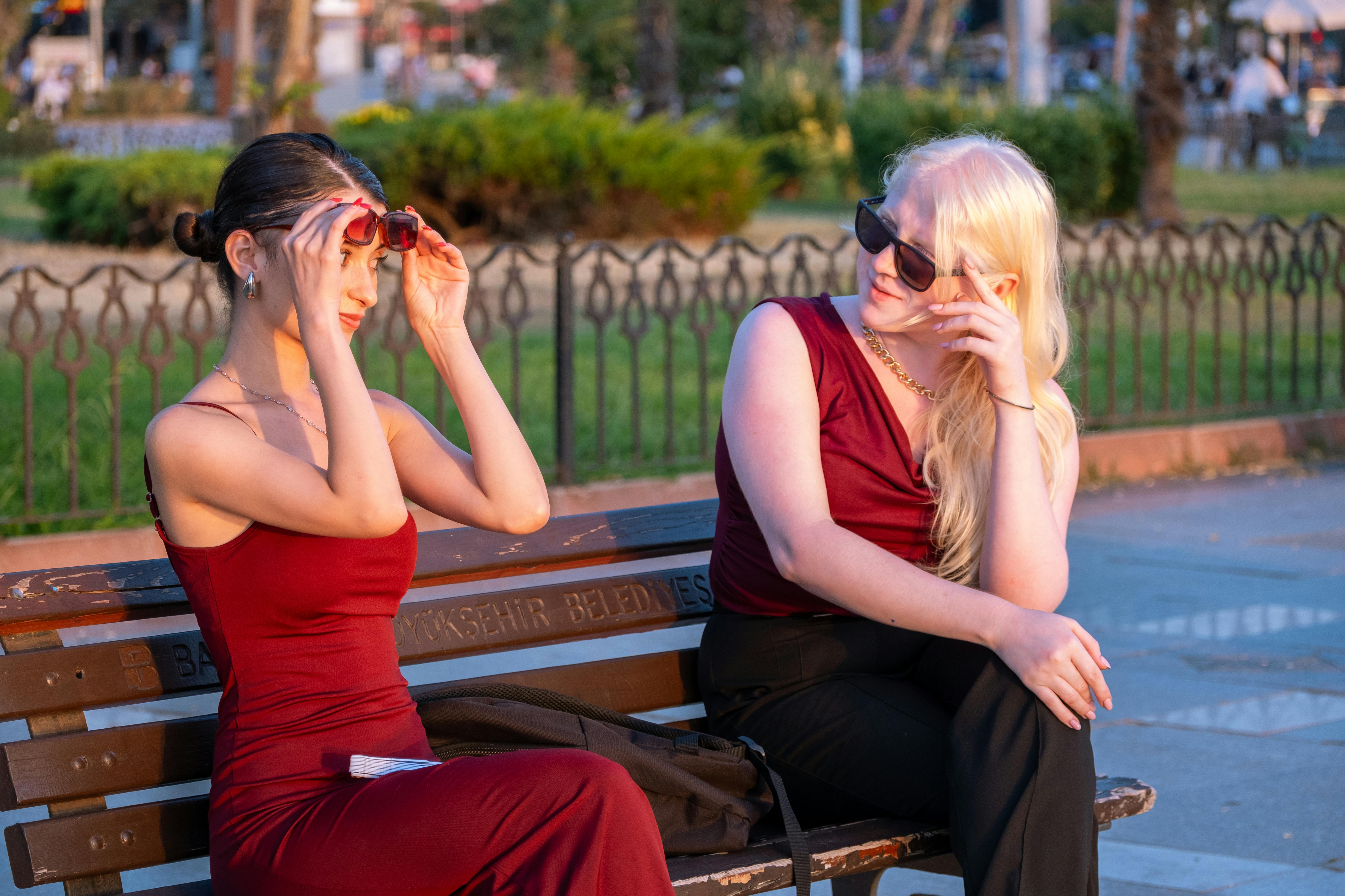 bezplatná Dvě ženy ve stylových oblecích si užívají slunečný den na lavičce v parku se slunečními brýlemi. Základová fotografie