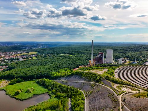 Free Aerial view of power plant surrounded by forests and clear skies, capturing nature-industry contrast. Stock Photo