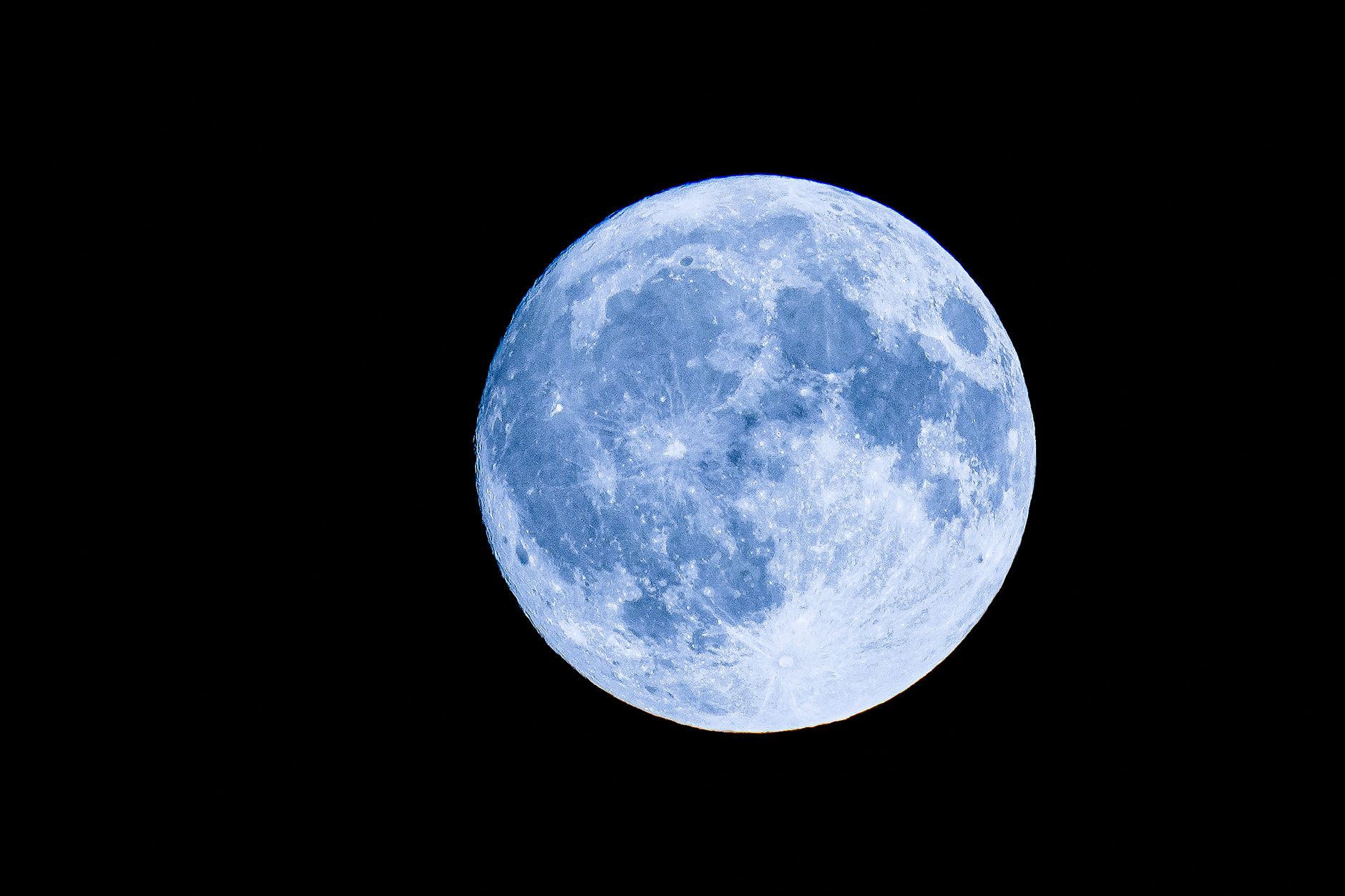 A detailed photo of a full moon with a vivid blue hue set against a black night sky.