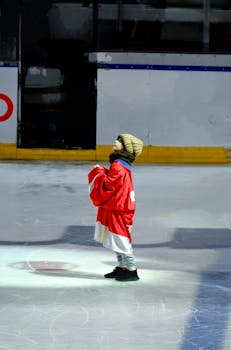 A child stands on an ice rink in a red hockey jersey, looking upward in anticipation.