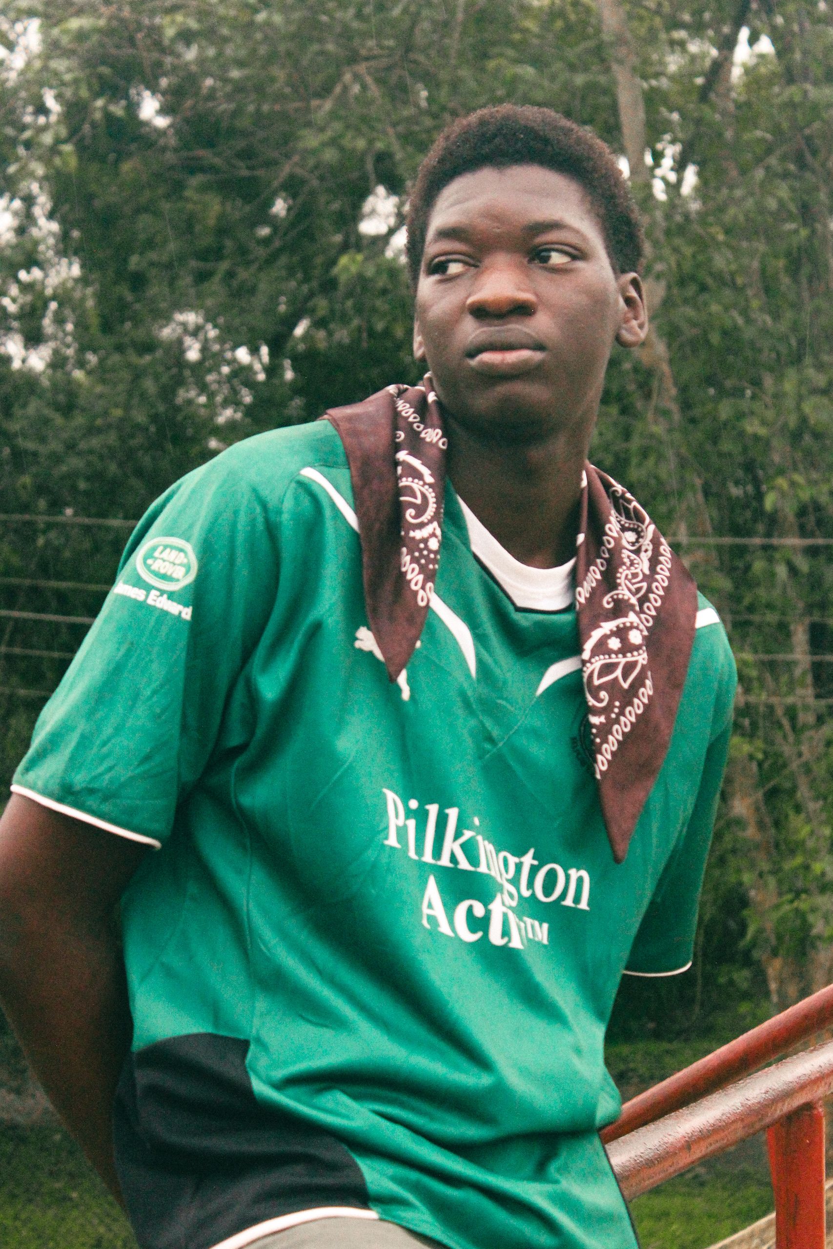 Portrait of a young man wearing a green soccer jersey, thoughtfully gazing outdoors.