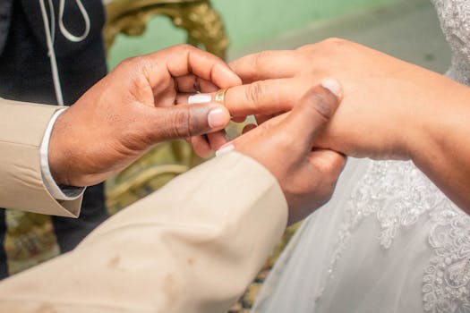 A close-up captures a groom placing a wedding ring on the bride's finger during their ceremony.