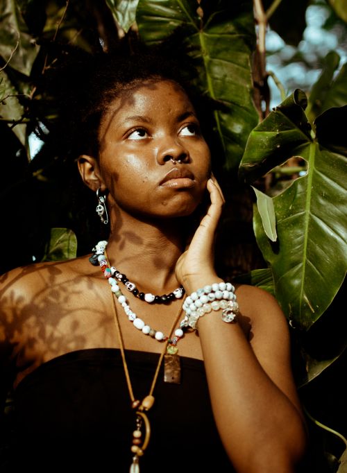 Free Portrait of a woman amidst lush greenery, wearing vibrant jewelry and looking contemplative. Stock Photo