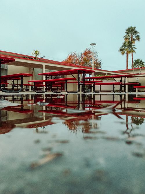 Free Red picnic tables reflected in a puddle after rain in San Jose, capturing an outdoor scene. Stock Photo