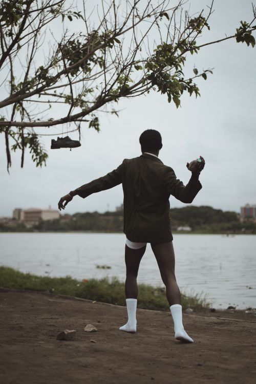 Free A man in formal attire stands by a river, holding a shoe, adding intrigue to the serene outdoor setting. Stock Photo