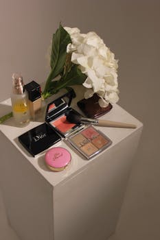 Aesthetic display of luxury makeup products with white hydrangea flowers on a pedestal.