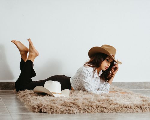 Free A young woman in a striped shirt and cowboy hat lies on the rug in a chic indoor setting. Stock Photo
