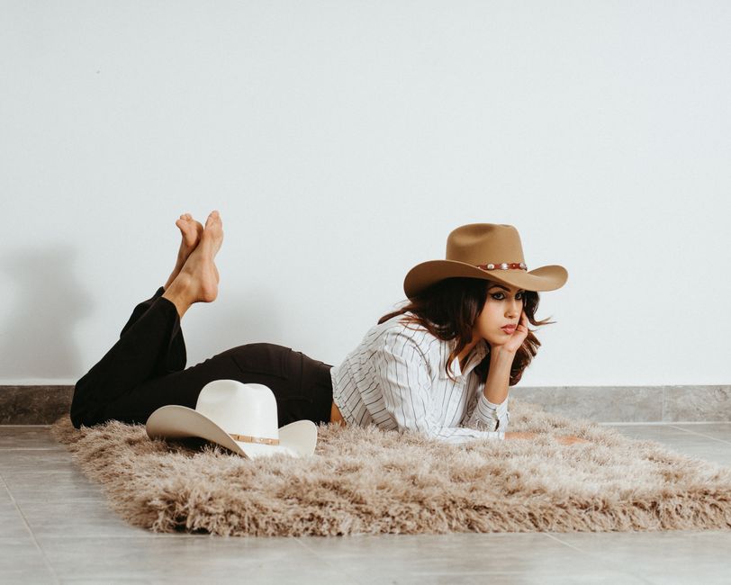 Coastal Cowgirl decor style interior — Woman in cowboy hat lying on rug in stylish indoor setting.