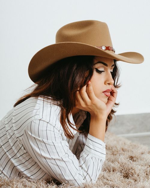 Free Woman lying on fluffy rug wearing a cowboy hat and striped shirt, exuding a relaxed vibe. Stock Photo