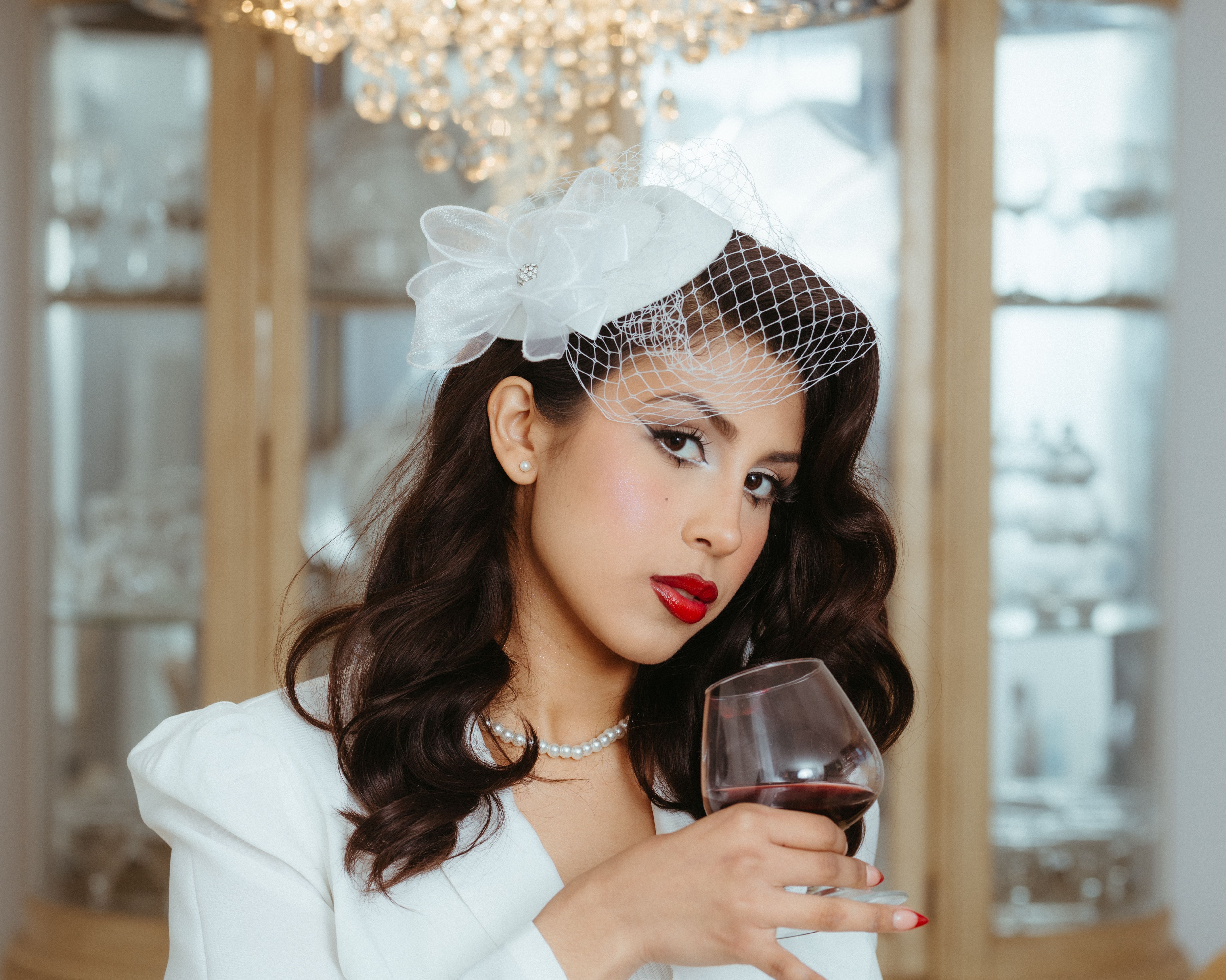 Stylish woman in white attire with a wine glass, elegant pose indoors.