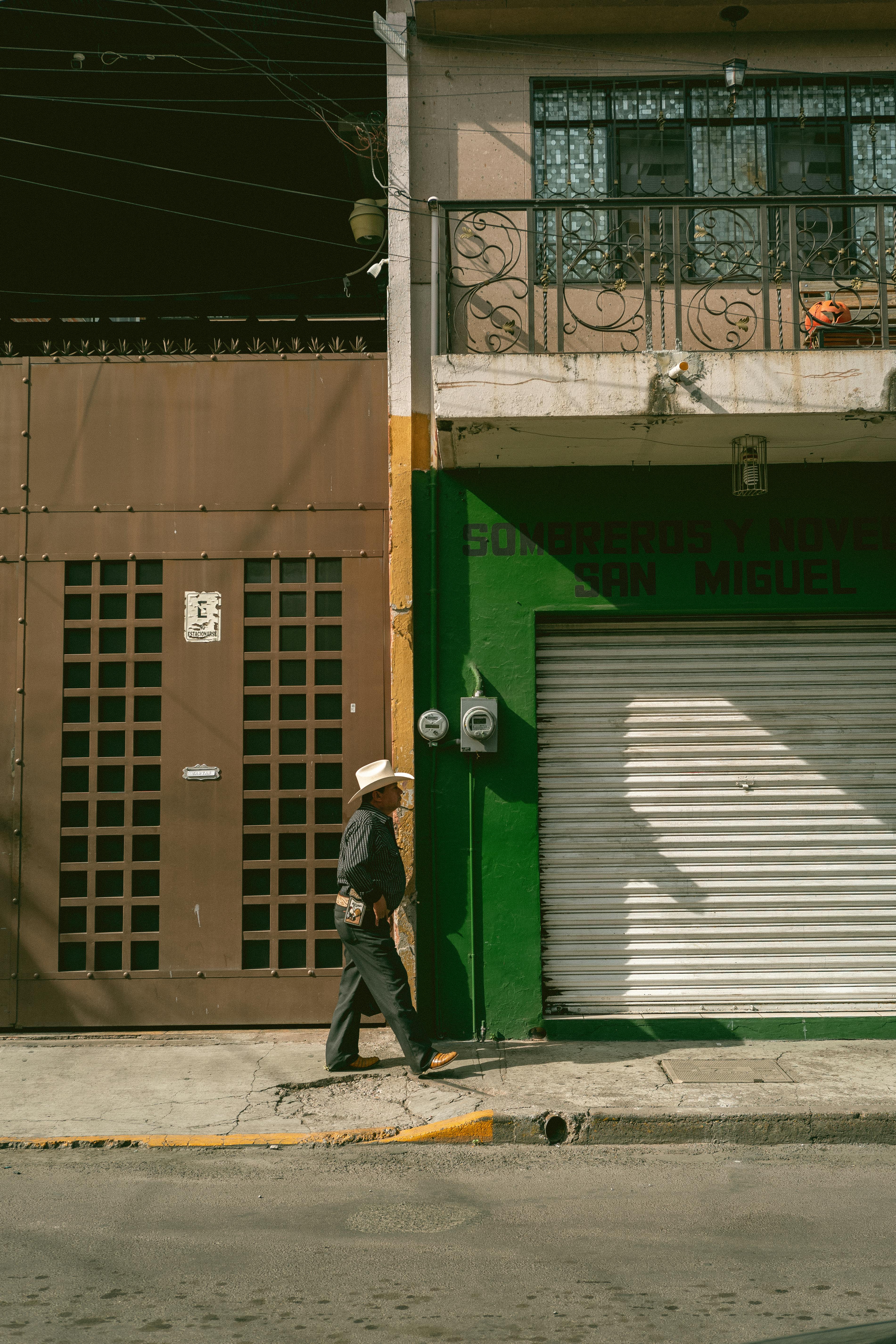 A man in a hat walks past a vibrant building facade in a sunlit urban street.