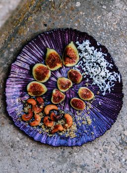 A beautifully arranged plate of figs, cashews, and coconut on a textured purple dish, creating a vibrant gourmet presentation.