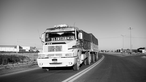 Black and white photo of a heavy duty truck on a rural road, conveying a sense of journey and transportation.