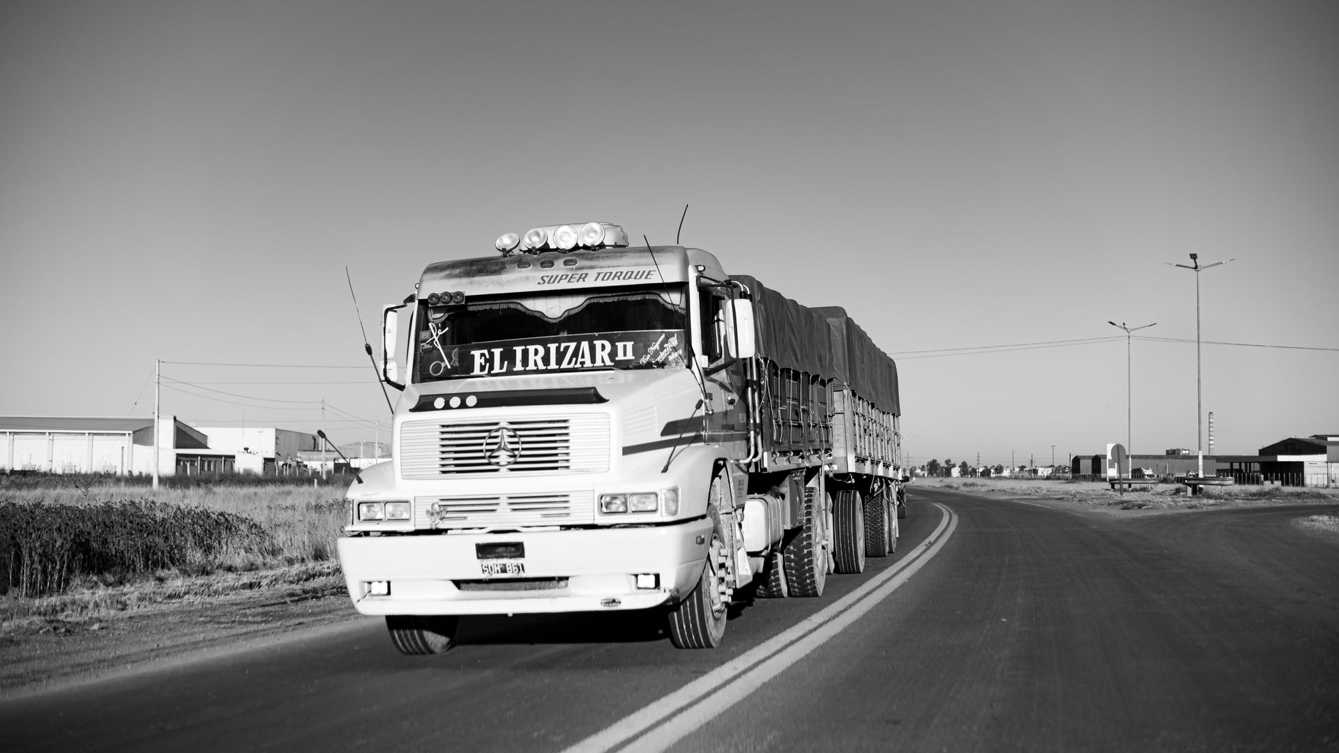 Black and white photo of a heavy duty truck on a rural road, conveying a sense of journey and transportation.