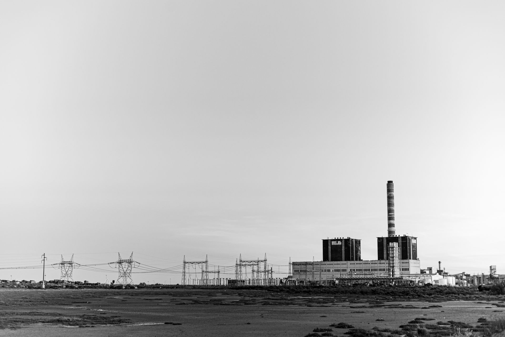 Black and white photo of a power plant with transmission lines, capturing urban industrial scenery.