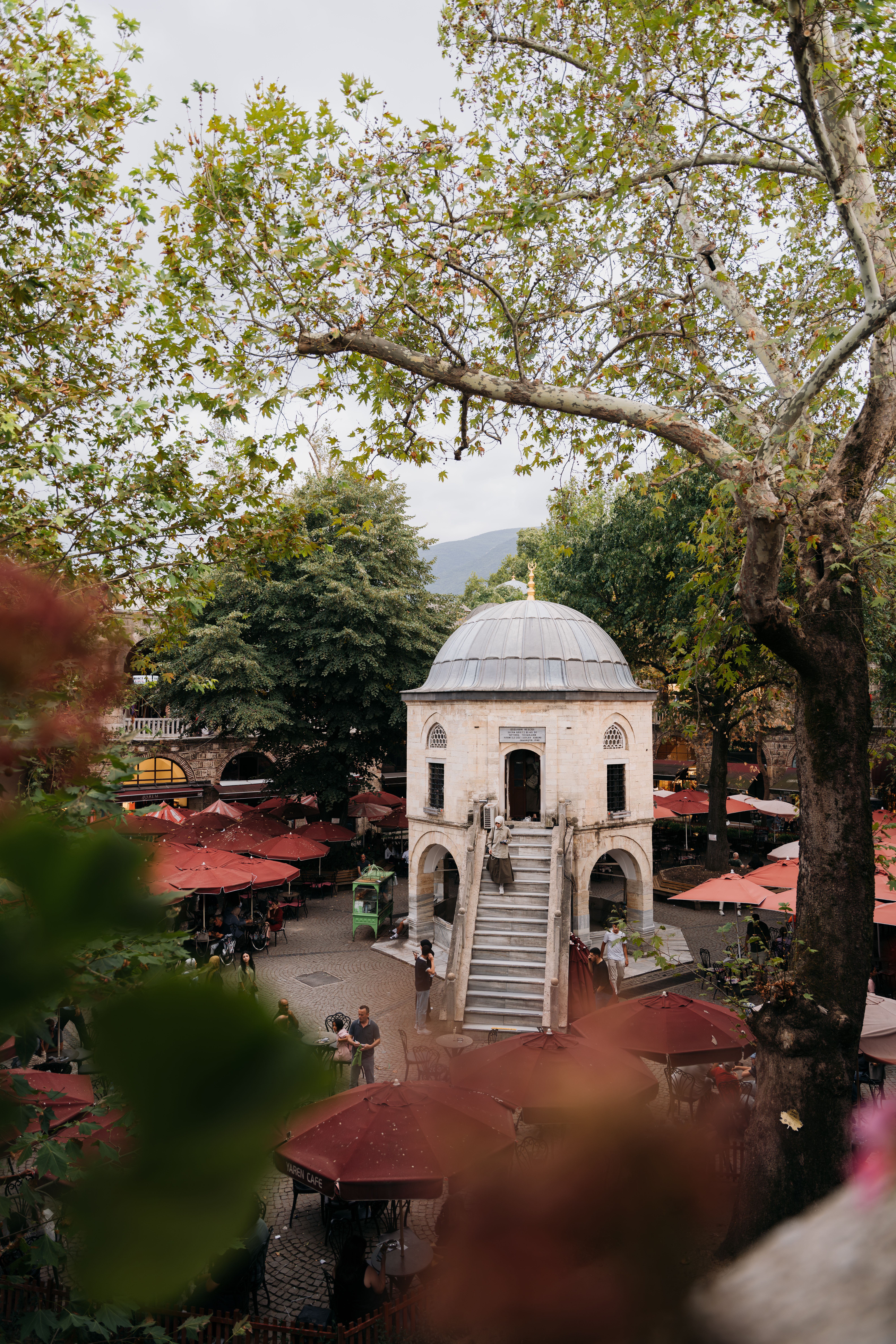 Charming Ottoman-era structure in lush park with outdoor cafes on a bright day.