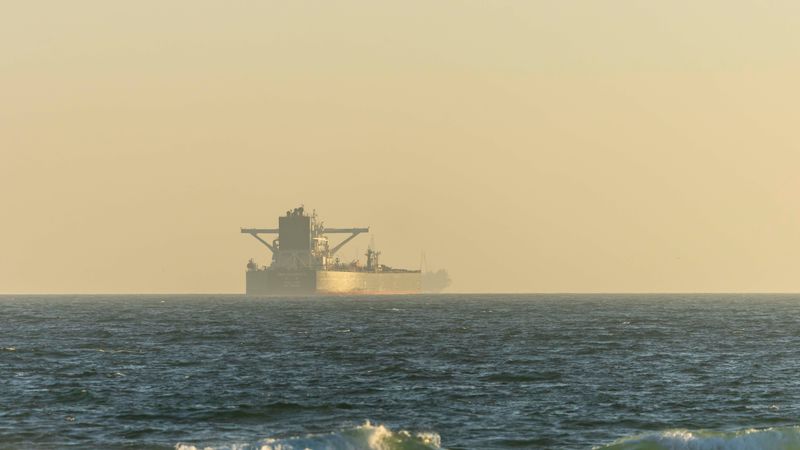 A cargo ship silhouetted against the horizon on a calm ocean during twilight.