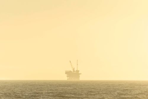 Free Distant view of an offshore oil platform against a golden sky at sunset over a calm sea. Stock Photo