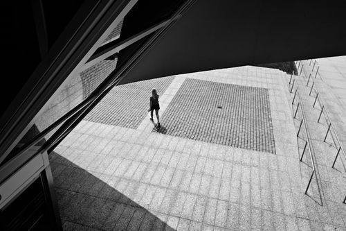 Free Dramatic black and white image of urban architecture featuring a solitary walker under sharp geometric shadows. Stock Photo